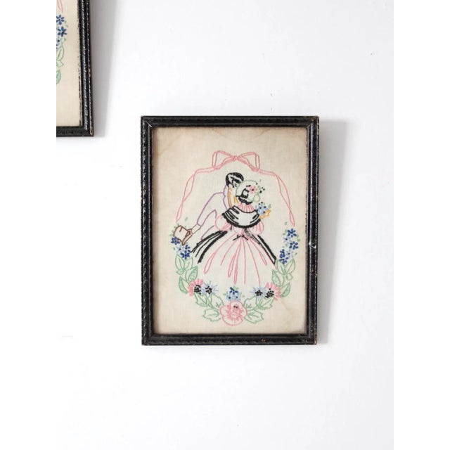 Pair of vintage framed embroidered textiles depicting a 19th century couple in shades of pink, green, blue, black, and...