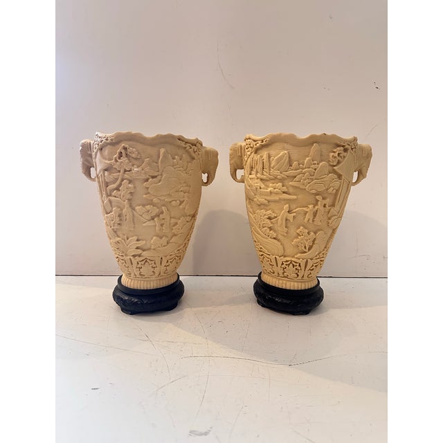 A pair of intricately carved vases crafted from a resin‑based composite material, featuring detailed relief scenes of...