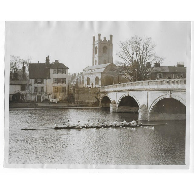 1928 black and white photo of the Cambridge University Crew Team rowing through Henley on Thames. Publication information...