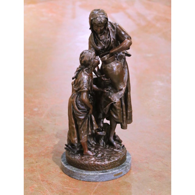 This elegant antique bronze sculpture titled À la Fontaine captures a tender rural moment between a young woman drawing...