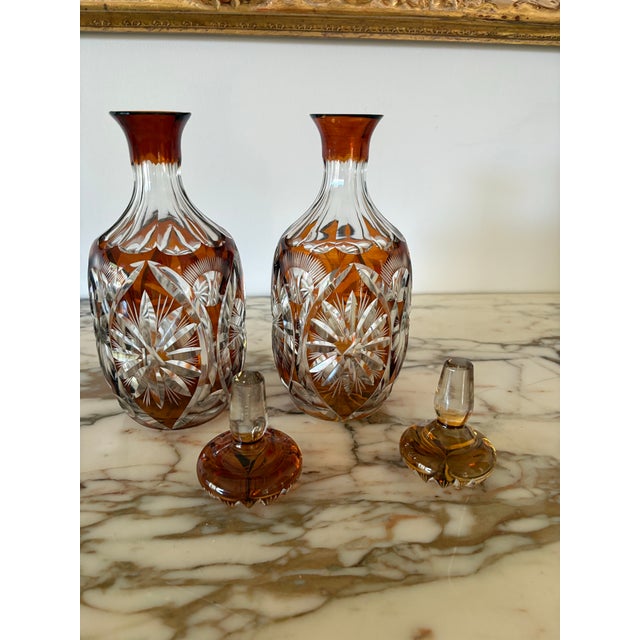 A pair of gorgeous Czech amber cut to clear crystal decanters. Both stoppers in tact with starburst pattern. Bottom of...