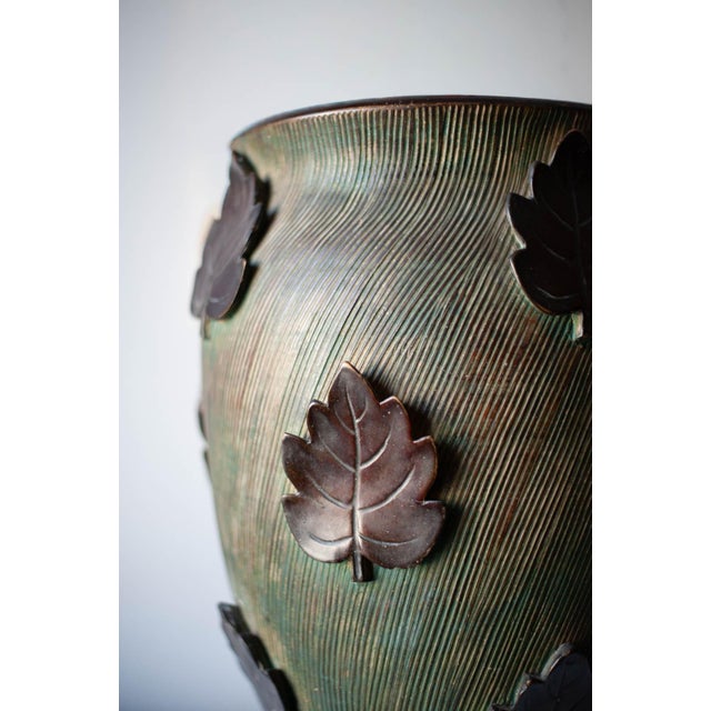 Ceramic vase characterized by a slightly flared shape and a surface worked with fine incisions. Decorated with leaf-shaped...