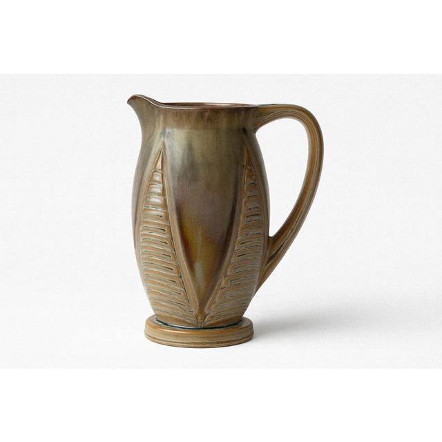 This French Art Deco pitcher by Denbac features stylized reliefs in a soft sage-green glaze. Its sculptural handle and...
