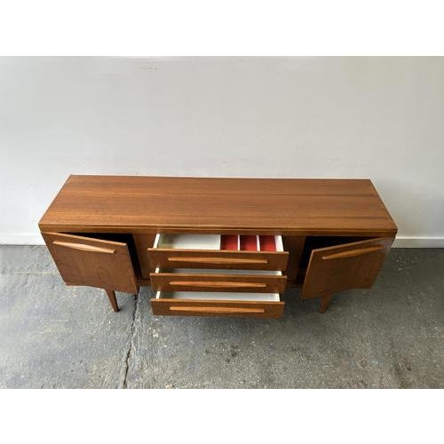 An English Mid-Century teak sideboard by recognised manufacturer Elliots of Newbury. Warm hued teak finish throughout with...
