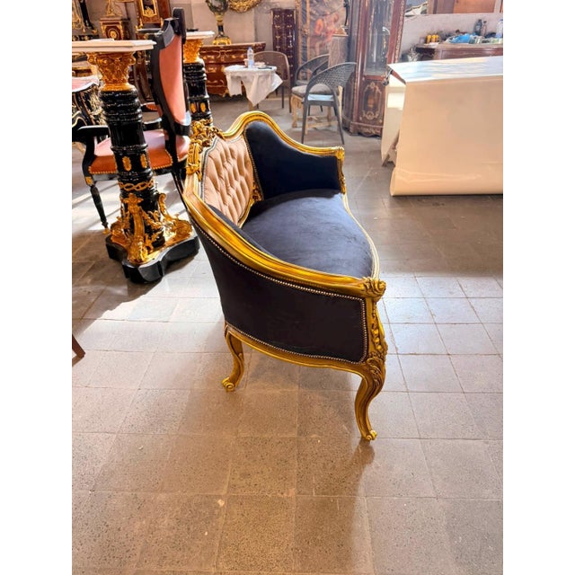 A dramatic French Louis XV-style canapé loveseat with a richly carved gilt frame, deep black upholstery, and a beautifully...