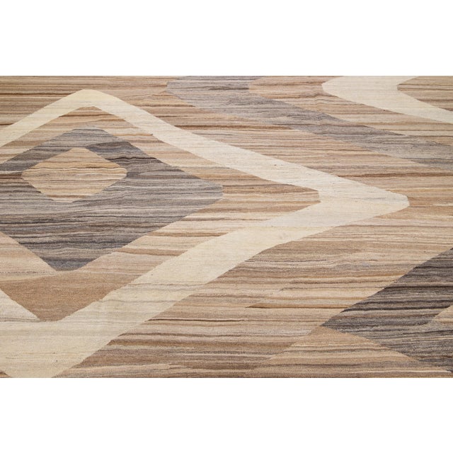 This flatweave wool rug boasts a striking light brown field and is accentuated with gray and beige hues. Its geometric...