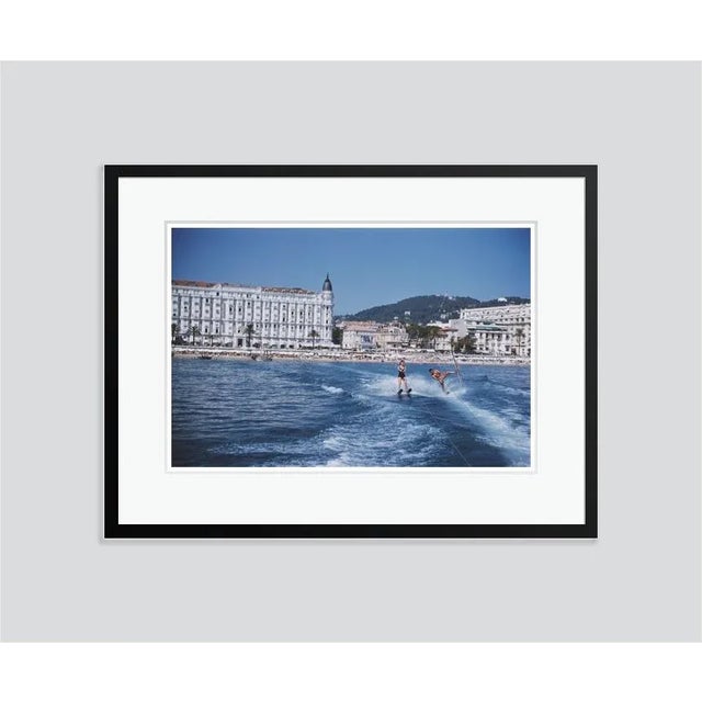 Cannes Watersports' by Slim Aarons Open Edition Holidaymakers waterskiing in front of the Carlton Hotel, Cannes, 1958....