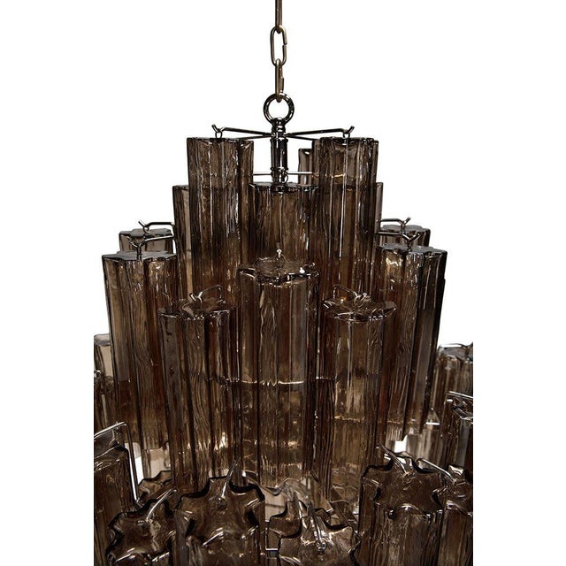This chandelier showcases a cascading, tiered design of textured glass arranged in staggered symmetry. Its smoked glass...