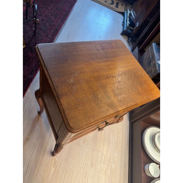 A charming French Louis XV style oak nightstand, defined by its elegant cabriole legs, softly scalloped apron, and carved...