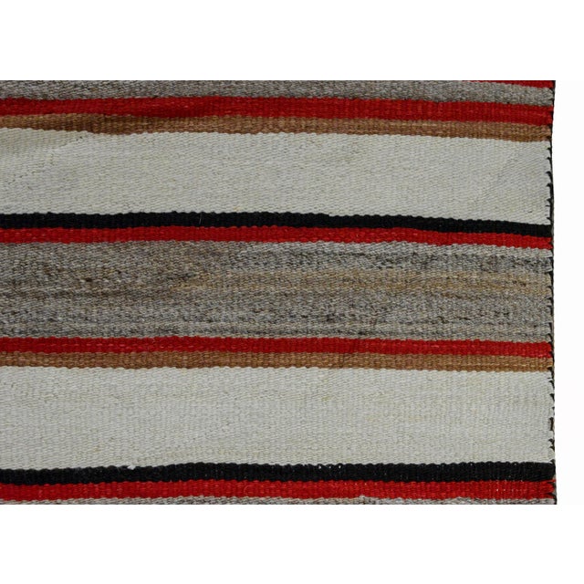 An early 20th century Native American Navajo style rug with red, gray, black, tan, and white stripes in the center, and...