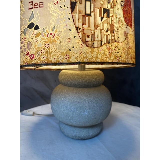 Elegant vintage lamp featuring a rounded gray ceramic base and a large fabric shade reproducing The Kiss, Gustav Klimt's...