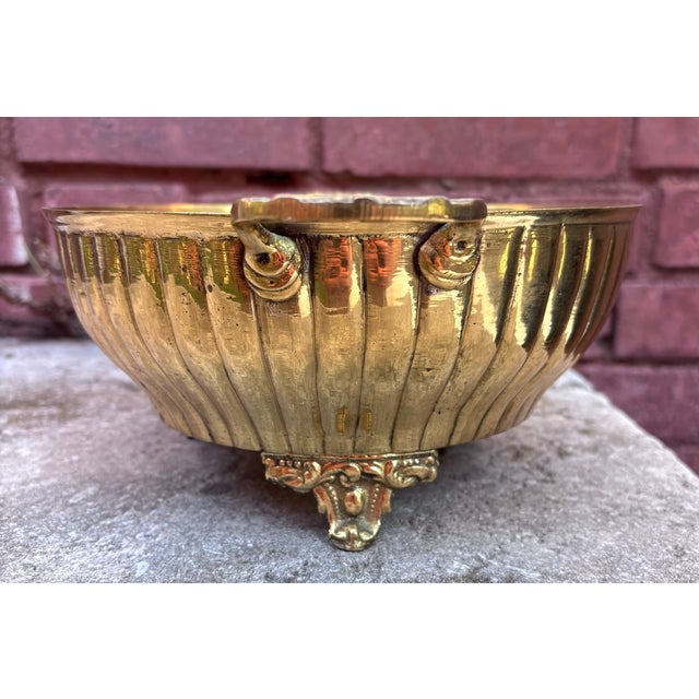 This is a vintage solid brass centerpiece or planter bowl featuring a ribbed body, decorative handles, and ornate feet....