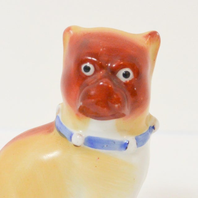 This exquisite, antique porcelain Pug dog is seated with open front legs. He is wearing a bright blue, ribbon collar...