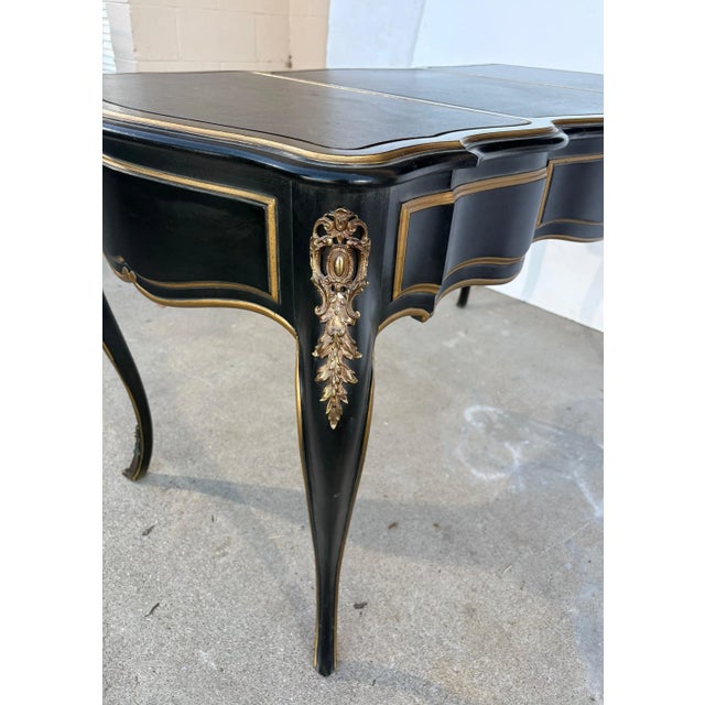 A Louis XV style writing desk. The top is faux leather with gold trim. It has three drawers and brass accents.