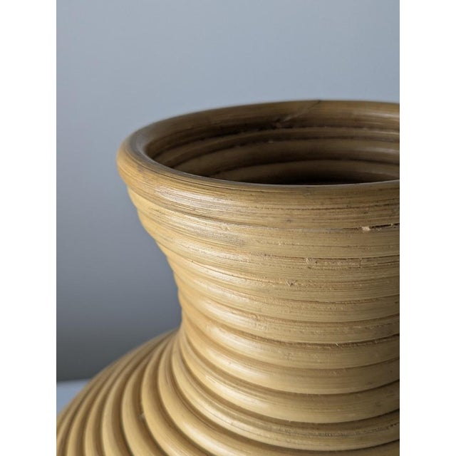 This large floor vase is constructed from continuously coiled natural rattan reeds, forming an amphora-inspired...