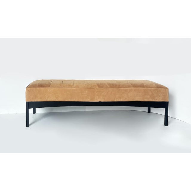 Close-up of a vintage bench in a light cognac color with Alcantara upholstery featuring an aged texture. The frame has...