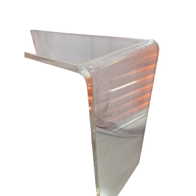 One clear acrylic waterfall table, a single bent sheet forming the top and both legs, at console or desk height. No maker...
