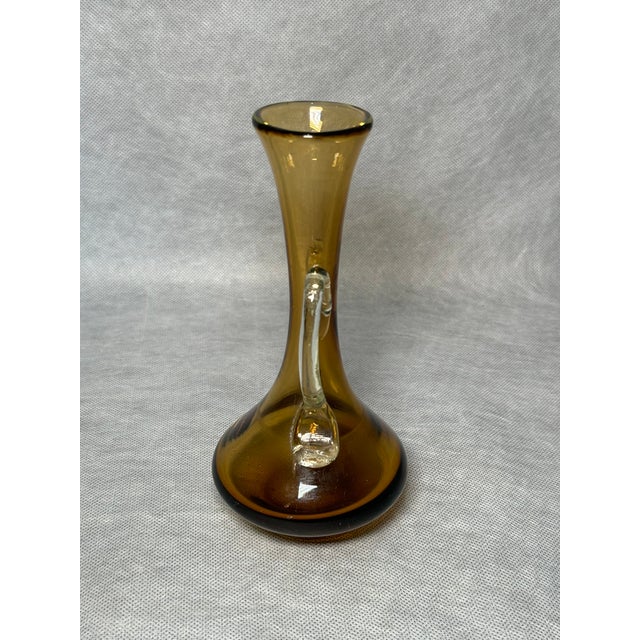 A slender 1960s uranium glass vase in a warm amber tone, featuring elegant applied handles. Its refined silhouette and UV-...