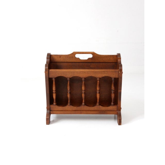 Vintage wooden magazine rack in an Early American style, featuring turned spindle sides and softly shaped panels. The warm...