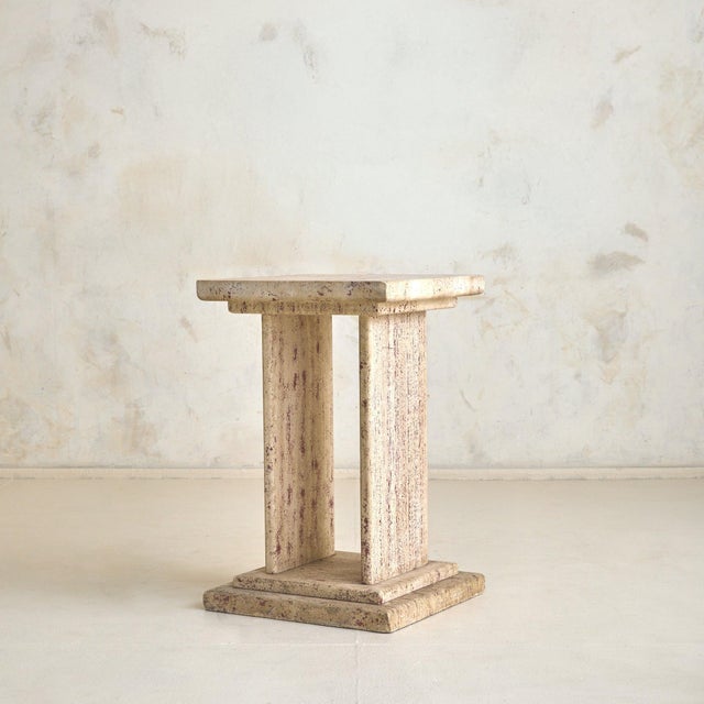 An Italian pedestal from the 1970s, sculpted from creamy travertine with visible pits, mineral inclusions, and subtle...