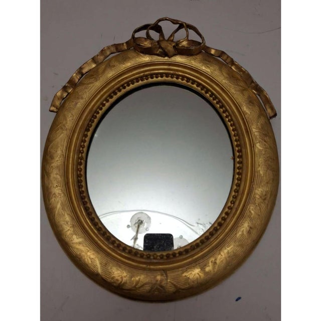 Elegant oval wall mirror in a finely carved and gilt wooden frame, decorated with engraved foliate and classical motifs...