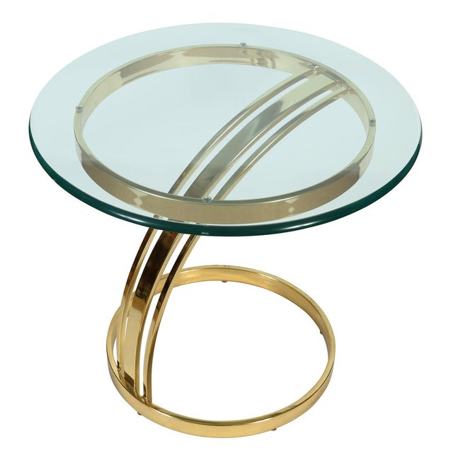 A sleek Milo Baughman style side table featuring a sculptural polished brass base and round glass top. The thick, beveled...
