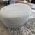 A large, oval upholstered ottoman/pouf. * Shape: Large oval/round, low-profile ottoman with a gently curved, almost drum-...