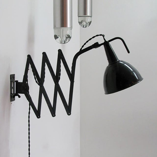 Articulating black enameled metal scissor wall lamps by Kandem, extends from 14″ to 50″, hood enameled white interior.