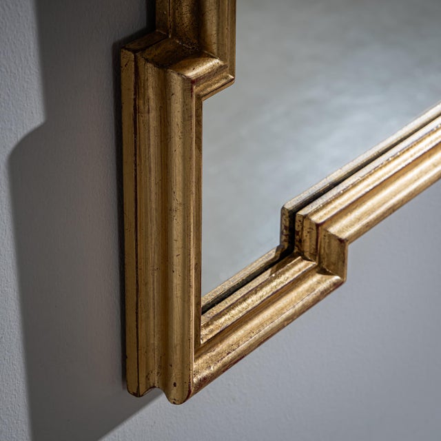 Wall mirror from the mid-20th century in a gold-patinated, profiled frame. The mirror is rounded and shows volute elements...
