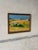 This landscape painting depicts a vibrant rural scene with golden fields, a distant mountain range, and a plane taking...