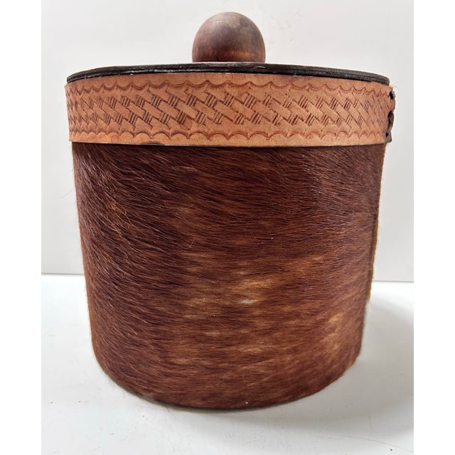 A handsome circa-1980s ice bucket wrapped in genuine cowhide and accented with hand-tooled leather detailing. The design...