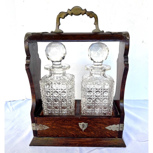Imported from England. Late 1800s tantalus set featuring two square cut crystal decanters housed in a lockable oak frame....