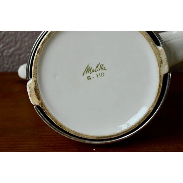 Modern and tapered look, this Melitta coffee maker is in white porcelain. His silver metal bell gives him a lot of style...