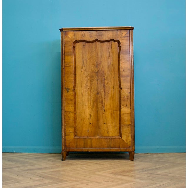 Biedermeier style single wardrobe in walnut veneer, dating to around the 1930s. Features a shaped moulded door with...