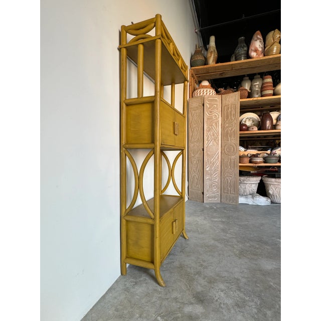 Beautiful Vintage bent rattan bookcase from the 1970s. The bookcase has 3 shelves and 2 closed space with doors, with...
