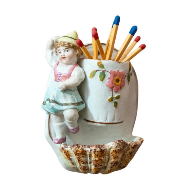 This unique wall-hanging porcelain match striker features a young German girl and a decorative floral motif. The shell...