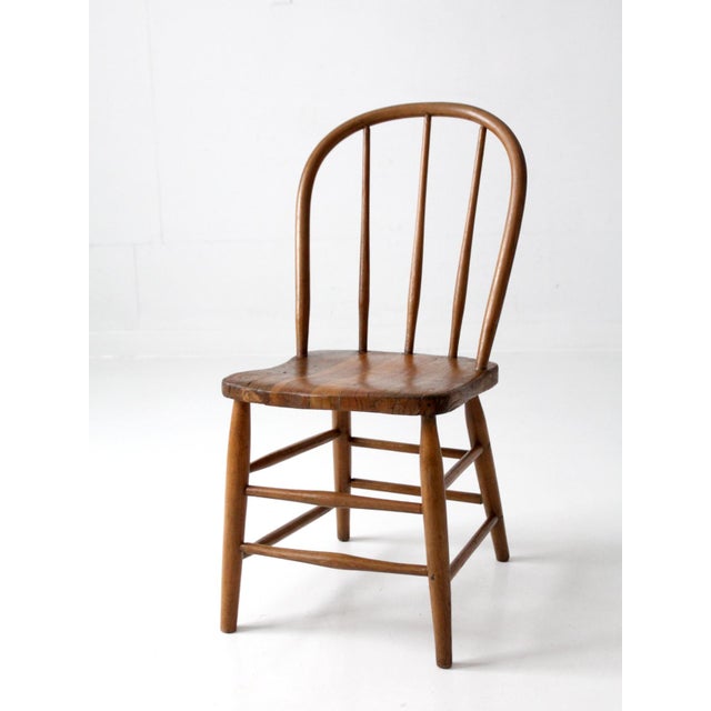 A vintage Windsor-style chair featuring the classic spindle-back silhouette and a solid wood seat with beautiful natural...