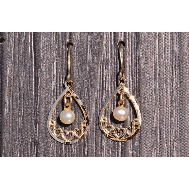 The Pala: Yellow Gold Dangler Earrings with Pearl. The earrings feature a central pearl which dangles below a pear shaped...