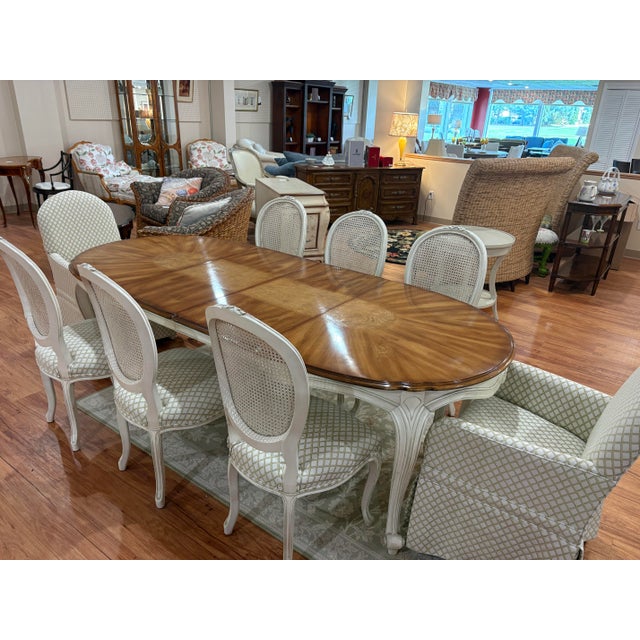 A graceful French Provincial dining set centered on a large oval table with a rich, warmly figured wood top featuring...