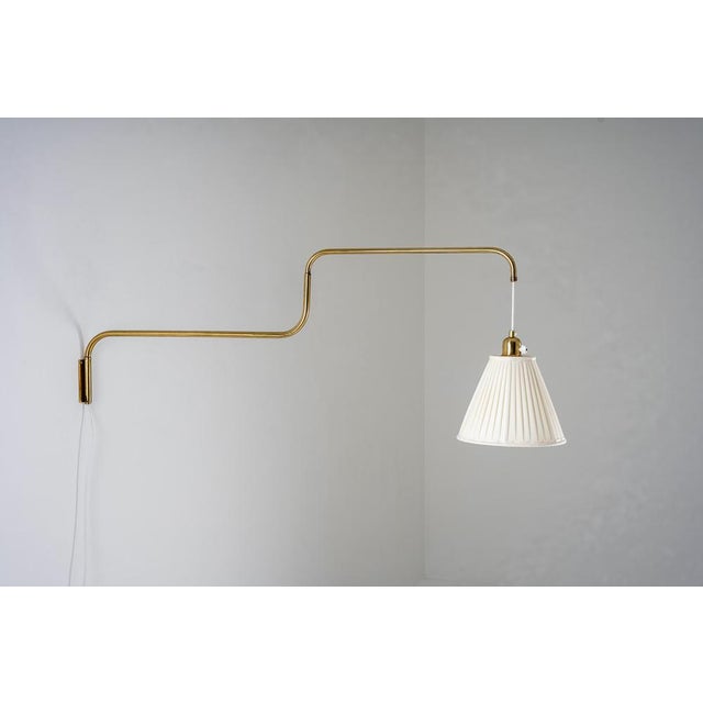 Elegant Swedish wall lamp executed in brass, defined by its elongated, sculptural arm with softly rounded bends. The...