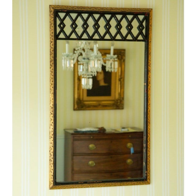 A rectangular gilt-framed wall mirror with a decorative black lattice or trellis pattern across the upper section, plain...
