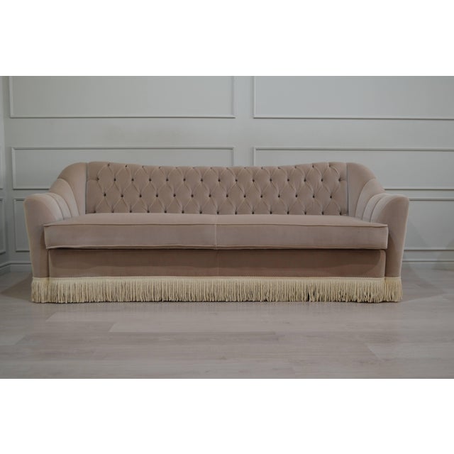 A glamorous vintage-inspired sofa featuring sculptural rounded arms, diamond-button tufting, and elegant cream fringe....