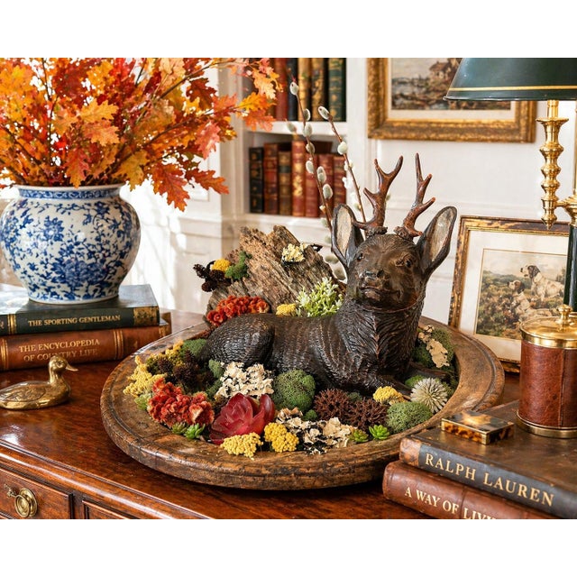 A striking vintage folk art composition featuring a hand-carved wooden stag nestled within a naturalistic woodland...