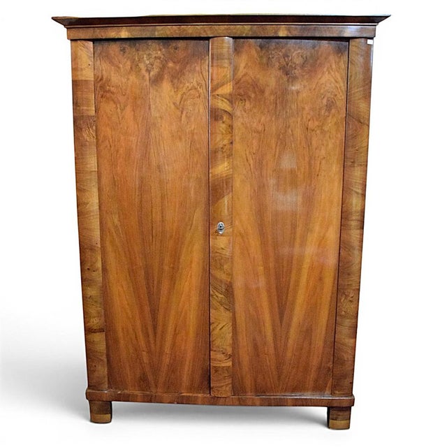 A Biedermeier-style wardrobe, crafted from solid wood and veneered with a beautifully grained, symmetrically patterned...