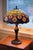 A spectacular and extra-large vintage Tiffany-style leaded glass lamp. The glass features a classic Art Nouveau peacock...