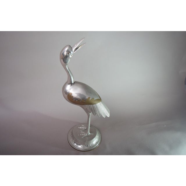 Vintage crane bird sculpture from the 1960s, in the Art Deco style. The silver-toned metal bird stands on one leg on a...