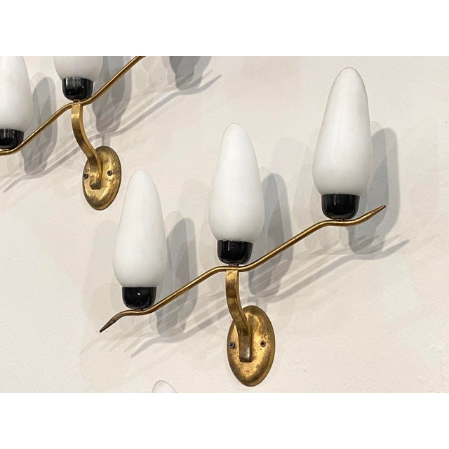 3 1960s wall sconces, gilt brass frame, black lacquered metal and white opal glass diffusers. This piece is designed in...