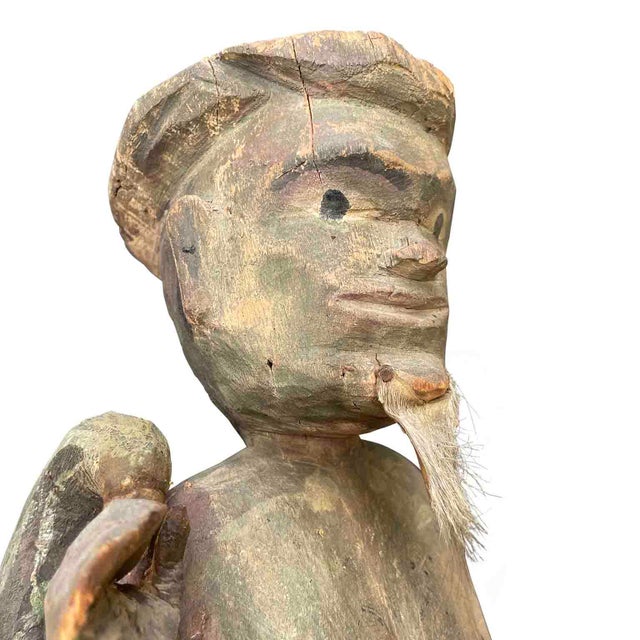 An antique Burmese shaman sculpture from the late 1800s, resting on a square base, is depicted standing with a staff in...