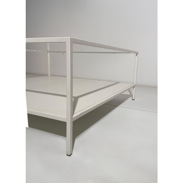 A rectangular coffee table with a minimalist and elegant design, featuring a simple white painted metal frame and two...