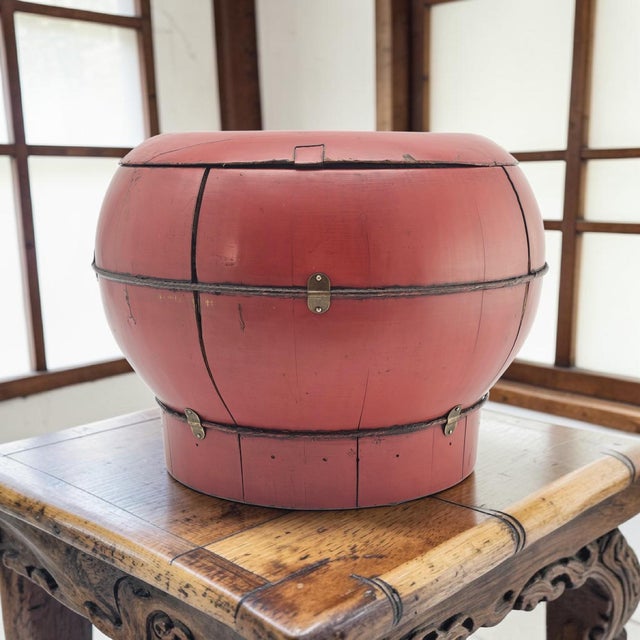 A traditional Chinese red lacquer rice bucket crafted from coopered wood staves and reinforced with metal bands. The...